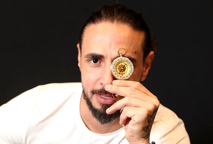 William Gutierrez segurando uma bússola dourada junto ao rosto
